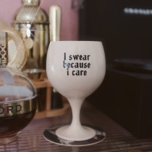 White wine glass with text 'I swear because I care' on a bar counter with a bottle of wine in the background.