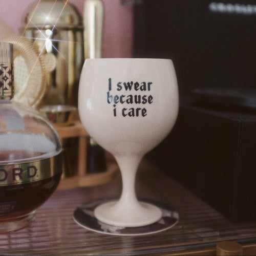 White wine glass with 'I swear because I care' text on a bar counter with bottles in the background.