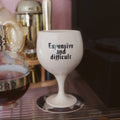 White wine glass with text 'Expensive and difficult' on a bar counter.